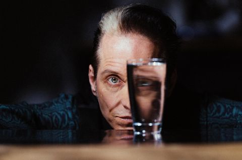 Bela B im Portrait. Vor seinem linken Auge steht ein Glas, durch das er blickt