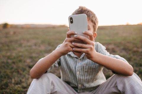 Ein Junge sitzt mit seinem Smartphone auf einer Wiese