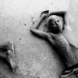 Straßenkind liegt auf dem Boden und schaut in die Kamera