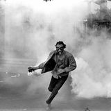 Demonstrant in Gasmaske wirft eine Tränengasgranate zurück in Richtung Polizei