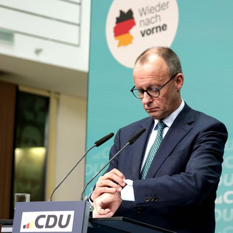 Friedrich Merz looks at his clock at a press conference.