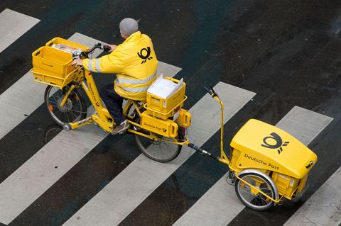 Symbolfoto zu Streik: Ein Postbote der Deutschen Post sitzt auf einem Fahrrad und fährt Briefe aus