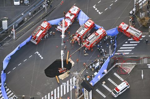 Mehrere Feuerwehr-Wagen stehen um ein Erdloch auf einer Kreuzung in Japan herum