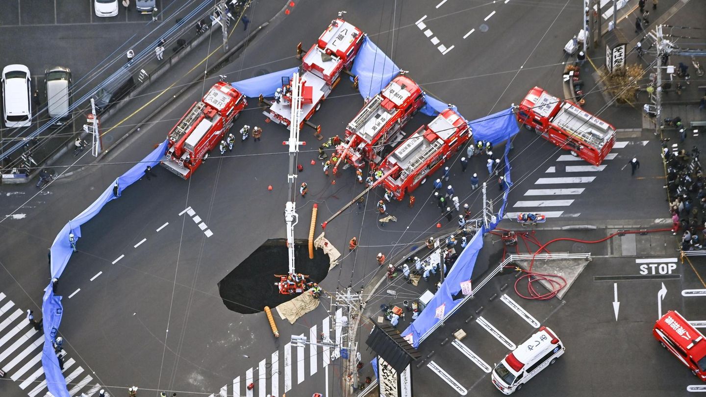 Mehrere Feuerwehr-Wagen stehen um ein Erdloch auf einer Kreuzung in Japan herum