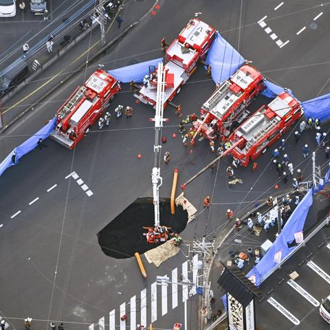 Mehrere Feuerwehr-Wagen stehen um ein Erdloch auf einer Kreuzung in Japan herum