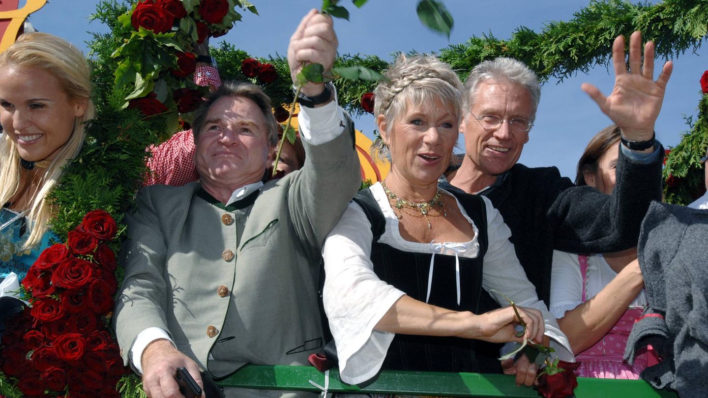 Robert Atzorn und seine Frau, die ein Dirndl trägt, winken von einem Oktoberfest-Wagen