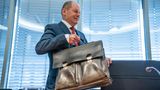 Olaf Scholz trägt seine Aktentasche und nimmt Platz