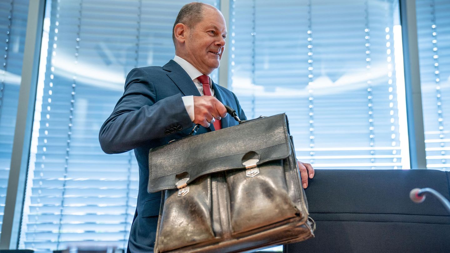Olaf Scholz trägt seine Aktentasche und nimmt Platz