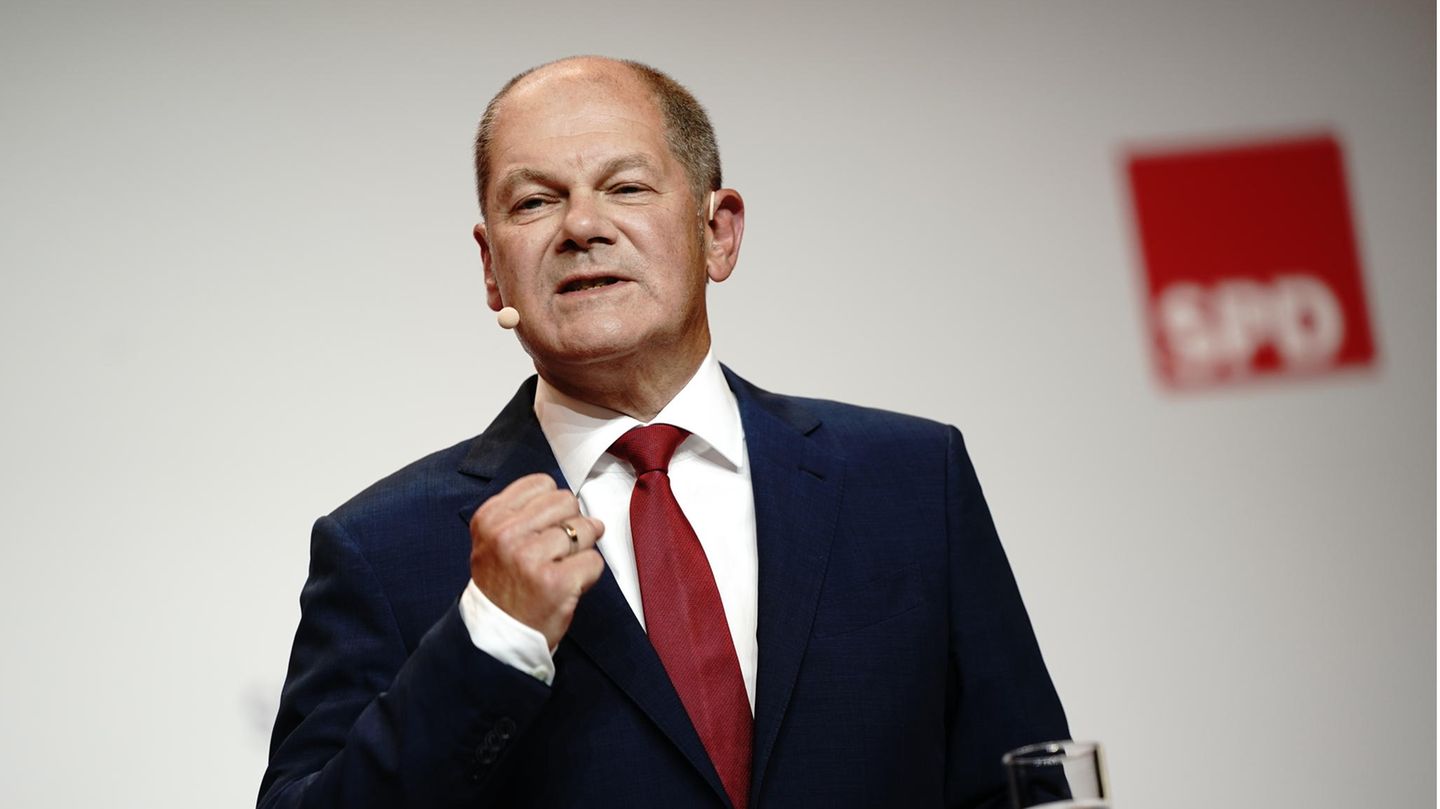 2020: Die Kanzlerkandidatur Olaf Scholz steht in schwarzem Anzug und roter Krawatte auf einer Bühne mit SPD-Logo und gestikuliert mit der rechten Hand