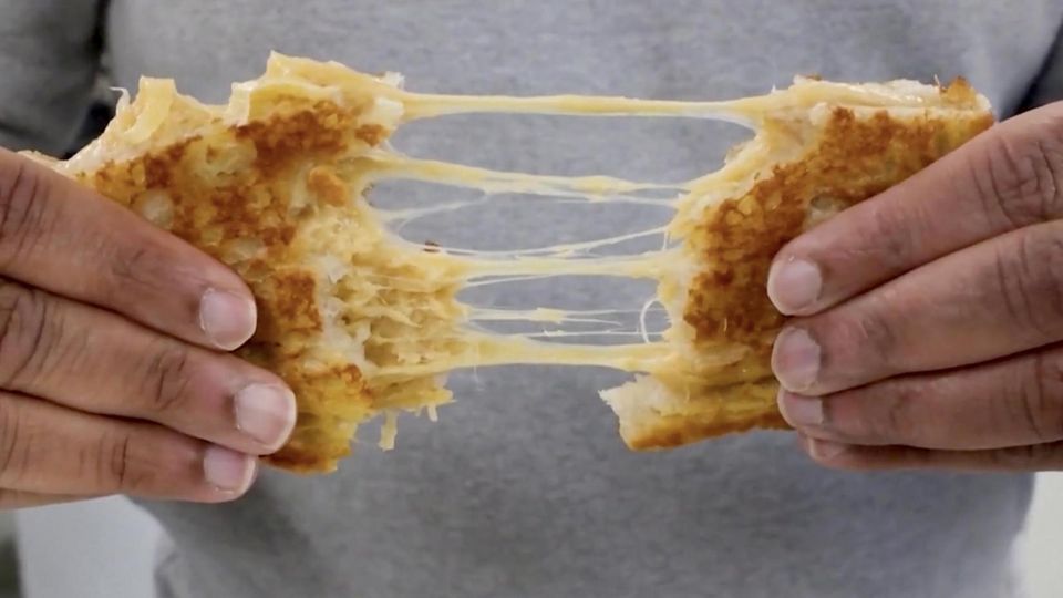 Ein Mann zieht ein Kunstkäse-Toast auseinander. Es entstehen ziehige Käseweben.