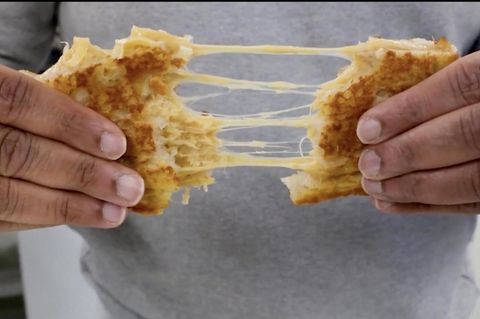 Ein Mann zieht ein Kunstkäse-Toast auseinander. Es entstehen ziehige Käseweben.