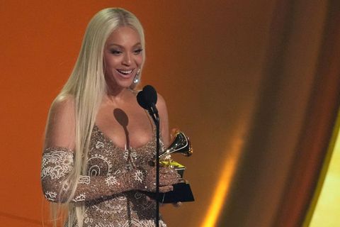 Beyoncé hält einen Grammy in beiden Händen und. spricht auf einer Bühne in ein Mikrofon