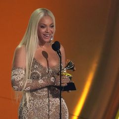 Beyoncé hält einen Grammy in beiden Händen und. spricht auf einer Bühne in ein Mikrofon