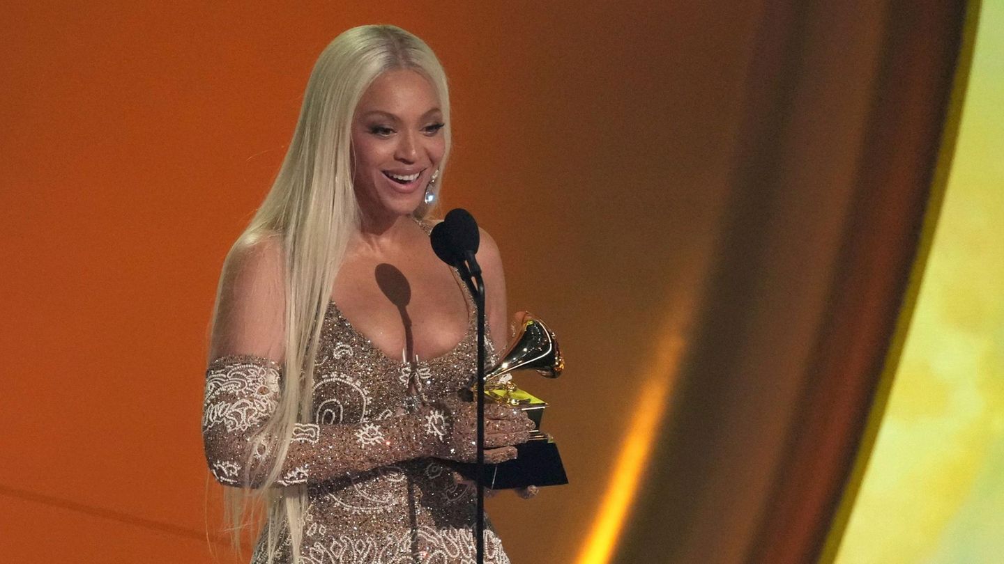 Beyoncé hält einen Grammy in beiden Händen und. spricht auf einer Bühne in ein Mikrofon