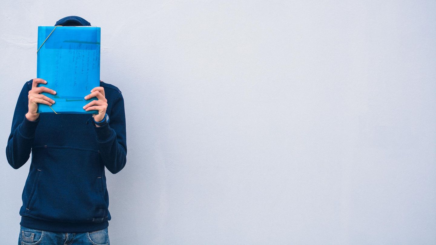 Mann verbirgt sein Gesicht hinter einer Aktenmappe