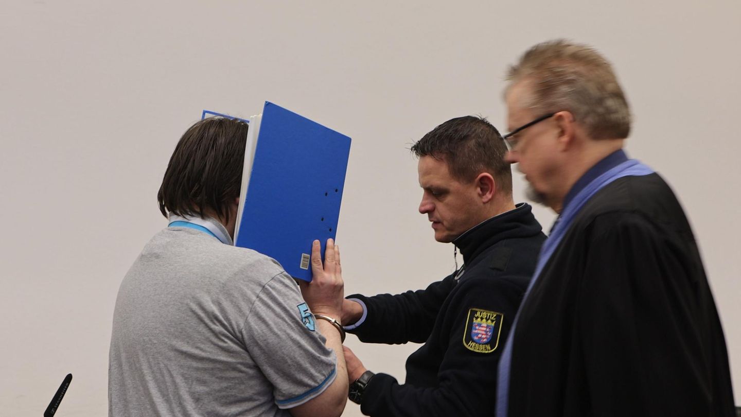 Der Angeklagte hält sich im Landgericht Gießen einen blauen Aktenordner vor sein Gesicht