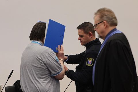 Der Angeklagte hält sich im Landgericht Gießen einen blauen Aktenordner vor sein Gesicht