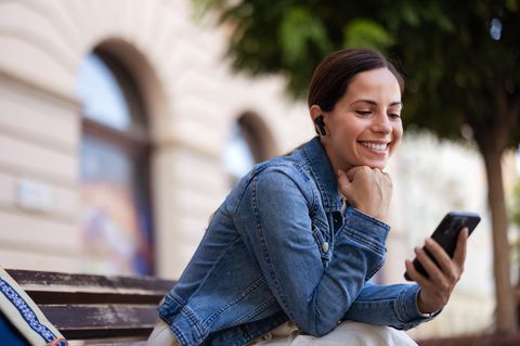 Entspannte Frau hört Musik mit kabellosen Ohrhörern und Mobiltelefon