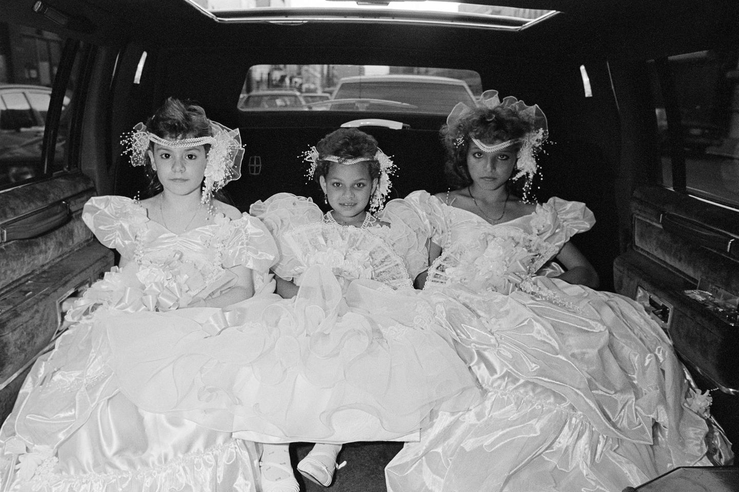 Wie kleine Prinzessinnen in Ballkleidern reihen sich diese drei Mädchen nebeneinander auf dem Rücksitz auf. Wohin sie wohl fahren?
