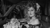 Eine Frau mit Blumen in den Haaren und Blumenstrauß auf dem Schoß auf dem Beifahrersitz