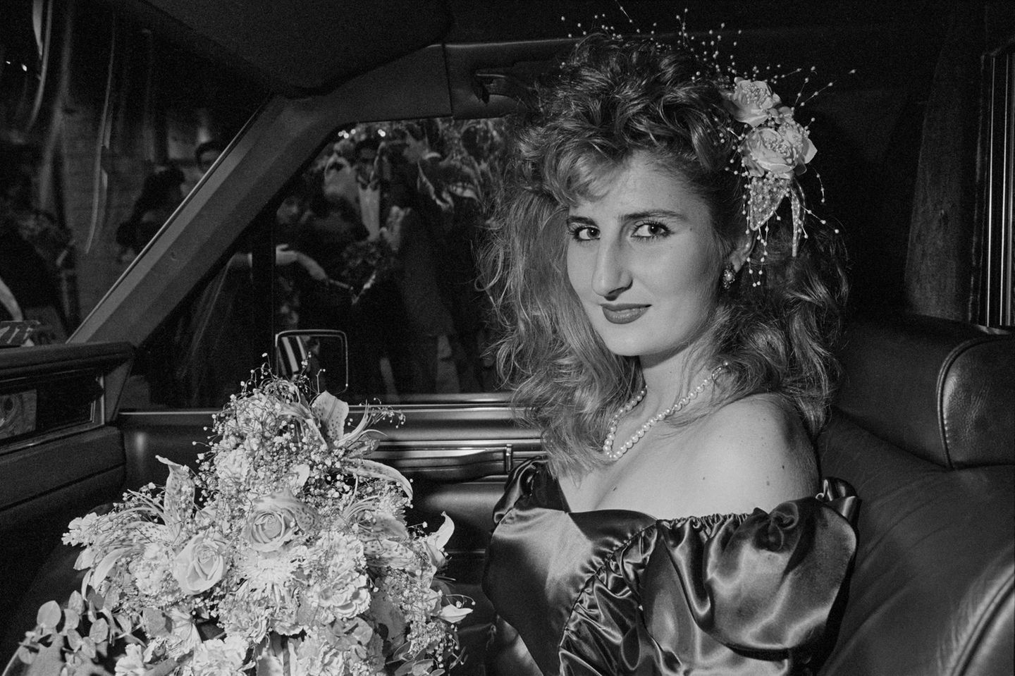 Eine Frau mit Blumen in den Haaren und Blumenstrauß auf dem Schoß auf dem Beifahrersitz