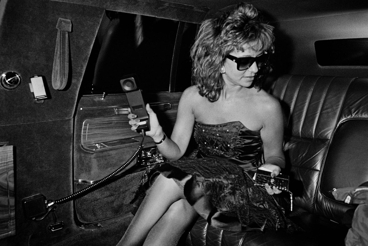 Eine Frau mit Sonnenbrille und Telefon in der Hand auf dem Rücksitz der Limousine