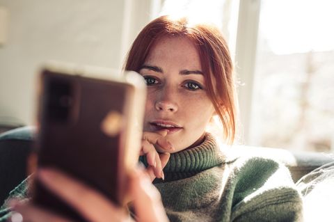 Eine junge Frau schaut auf ihr Smartphone und nutzt Whatsapp