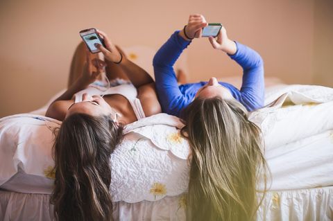 Internetsucht: zwei junge Frauen liegen auf einem Bett und schauen auf ihre Smartphones
