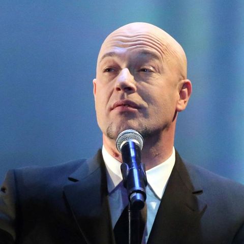 Der Graf von Unheilig singt im dunklen Anzug vor einem blauen Bühnen-Hintergrund in ein Mikro