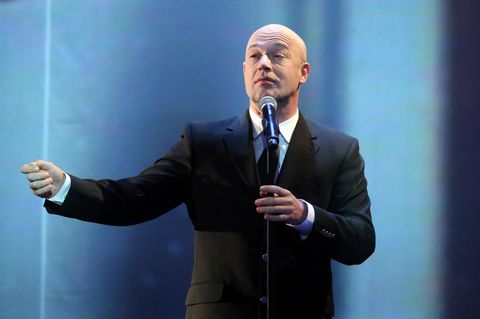 Der Graf von Unheilig singt im dunklen Anzug vor einem blauen Bühnen-Hintergrund in ein Mikro