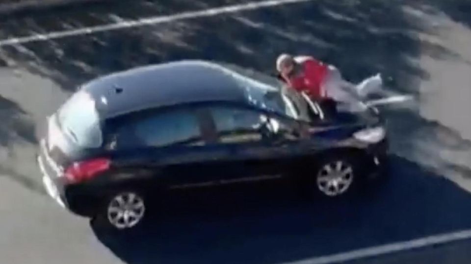 Video zeigt: Fahrer flüchtet nach Unfall mit anderem Beteiligten auf Motorhaube Ein schwarzes Auto fährt mit einem Mann auf der Motorhaube auf einer Bundesstraße