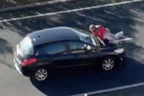 Ein schwarzes Auto fährt mit einem Mann auf der Motorhaube auf einer Bundesstraße