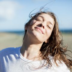 Bebilderung "Sinn finden im Leben": Eine Frau steht mit geschlossenen Augen und zufriedenem Blick am Strand