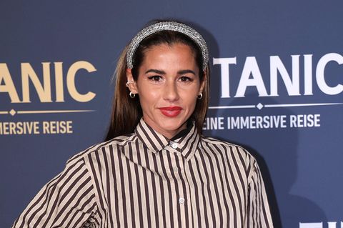 Sarah Engels steht mit Glitzerhaarreifen und schwarz-weiß gestreifter Bluse auf dem Red Carpet und lächelt