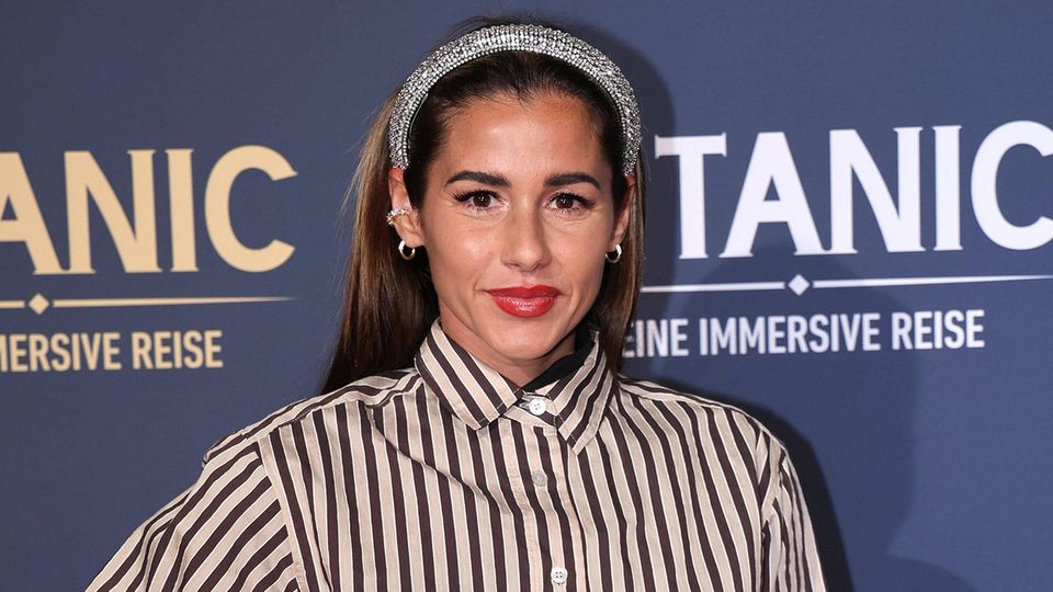 Sarah Engels steht mit Glitzerhaarreifen und schwarz-weiß gestreifter Bluse auf dem Red Carpet und lächelt