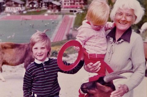 Eine lachende Großmutter mit zwei Enkelinnen, die sie der Gewohnheit nach an der Hand hält.