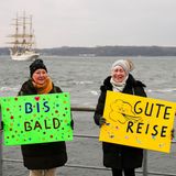 Die Hamburgerin Edeltraut Reim (r) und ihre Schwester Claudia Wagner stehen während des Auslaufens der "Gorch Fock" im Marinehafen mit Schildern, auf denen "Gute Reise" und "Bis bald" steht