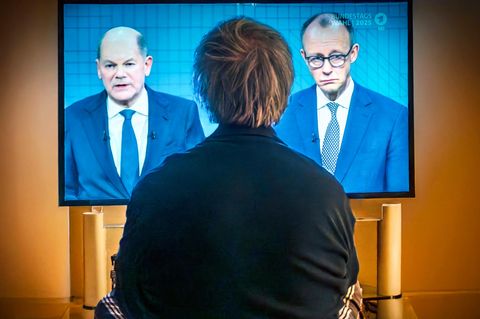 Eine Person schaut auf einem Fernseher das TV-Duell zwischen Scholz und Merz