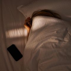 Eine Frau schläft, während ihr Smartphone neben ihr im Bett liegt