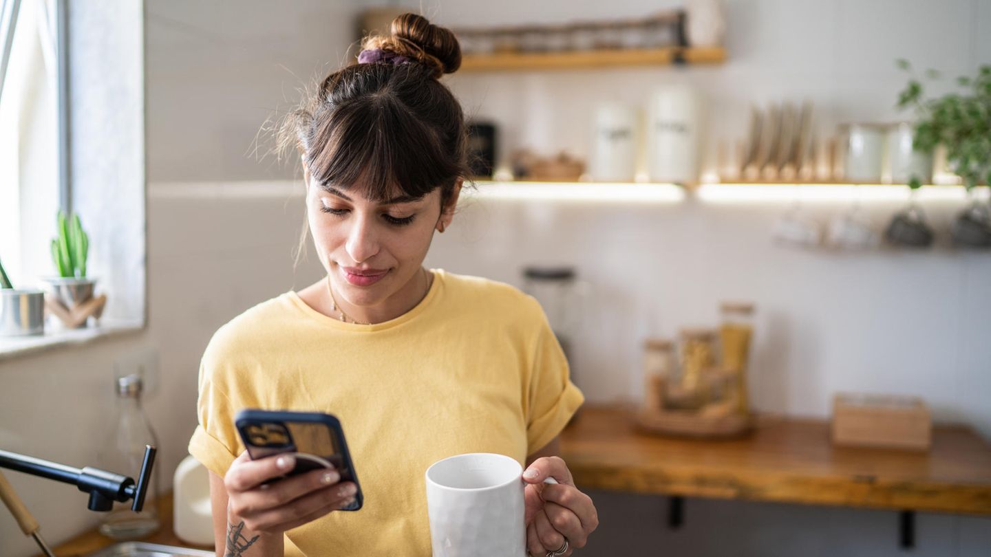 Eine Frau schaut in der Küche auf ihr iPhone