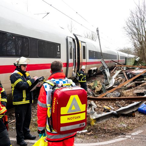 Einsatzkräfte stehen an der Unfallstelle des ICE an einem Bahnübergang