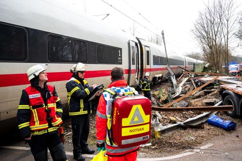 Einsatzkräfte stehen an der Unfallstelle des ICE an einem Bahnübergang