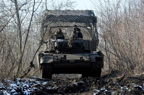 Vier ukrainische Soldaten sitzen auf einem getarnten Panzer im Wald