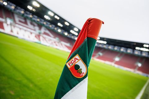 Das Logo vom FC Augsburg auf der Eckfahne vor dem leeren Stadion