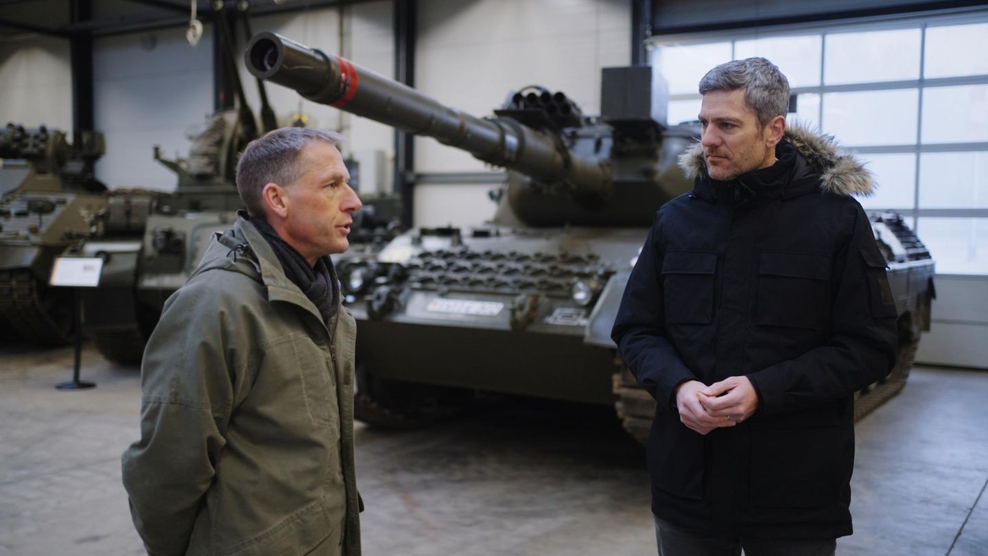 Ingo Zamperoni steht vor einem Panzer und spricht mit Ulrich Nothwang, einem Reservisten in olivgrüner Jacke
