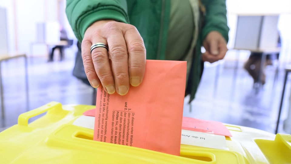 Direktwahlbüros helfen im Wahlvorgang: "Wir sorgen dafür, dass Ihre Stimme zählt" Ein Mann steckt einen rosafabrigen Umschlag in einer Wahlurne