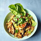 Udon-Nudeln mit gerösteten Auberginen     Für 1 Person  1 Aubergine (250g)   1 Knoblauchzehe   1 Pak Choi   1 EL geröstete ungesalzene Erdnusskerne   1 EL süße Chilisauce  150g Instant-Udon-Nudeln (aus dem Asia-Laden)  4 Frühlingszwiebeln   1⁄2 frische rote Chilischote   1⁄2 Romanasalatherz   2 Stängel Minze oder Koriandergrün  1 EL Crunchy Erdnuss & Sesam- Chiliöl (Knusper-Chiliöl mit Sesam & Erdnussstückchen)  1 EL Balsamico-Essig     Vorbereitung 7 Minuten   Garzeit 20 Minuten   1 Schublade   Die Auberginen der Länge nach in 1cm dicke Scheiben und dann in lange 1 cm breite Streifen schneiden. Den Gitterboden aus der Airfryer-Schublade entfernen, die Auberginenstreifen hineingeben und 15 Minuten bei 200°C garen. Nach der Hälfte der Zeit durchrühren.Den Knoblauch schälen und in feine Scheiben schneiden.Den Pak Choi längs vierteln. Wenn die 15 Minuten vorüber sind, die Schublade herausziehen, den Knoblauch und die Erdnüsse über die Auberginen streuen, die süße Chilisauce über das Gemüse träufeln und durch Rütteln der Schublade gleichmäßig verteilen. Seitlich den Pak Choi einlegen und weitere 5 Minuten bei 200 °C garen, bis die Aubergine weich und sämig ist.In einer Schüssel die Udon-Nudeln mit kochendem Wasser bedecken und quellen lassen. Die Frühlingszwiebeln putzen und in feine Scheiben schneiden, die halbe Chili in Ringe schneiden. Die Salatblätter trennen, die Kräuter abzupfen.Die Nudeln abgießen und mit dem größten Teil der Frühlingszwiebeln und der Chili sowie dem Chiliöl und dem Essig zu dem Gemüse in die Schublade geben. Alles gut vermengen, sorgfältig abschmecken und auf einem Teller anrichten. Die Salatblätter daneben platzieren, alles mit den restlichen Chilis, Frühlingszwiebeln und mit den Kräutern garnieren und servieren.