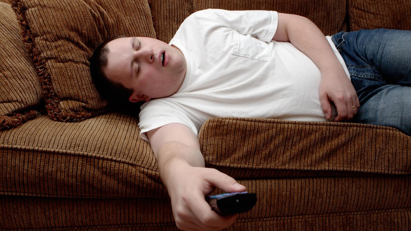 Mann schläft mit Fernbedienung auf Sofa