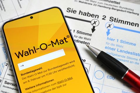 Ein Smartphone mit geöffneter Wahl-O-Mat-Internetseite liegt auf einem Stimmzettel. Daneben liegt ein Kugelschreiber
