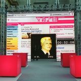 Die virtuelle Figur Robert von T-Online im Bildschirm neben dem ehemaligen Vorstandsvorsitzenden Wolfgang Keuntje (r.)